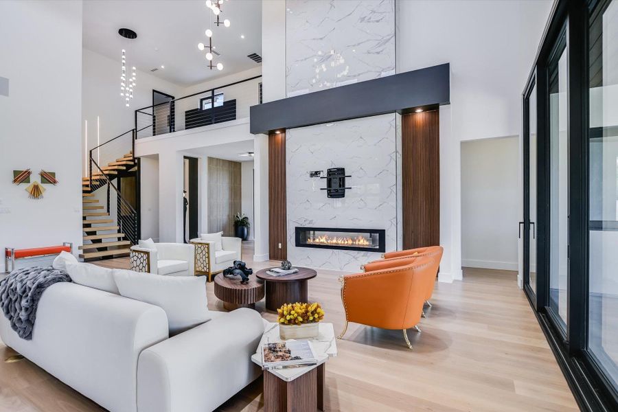 Living area featuring a high ceiling, open floating stairway, wood finished floors, and a stunning marble fireplace Living area featuring a high ceiling, open floating stairway, wood finished floors, and a stunning marble fireplace