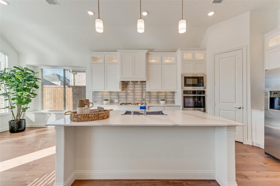 Kitchen featuring appliances with stainless steel finishes, white cabinetry, decorative light fixtures, and tasteful backsplash