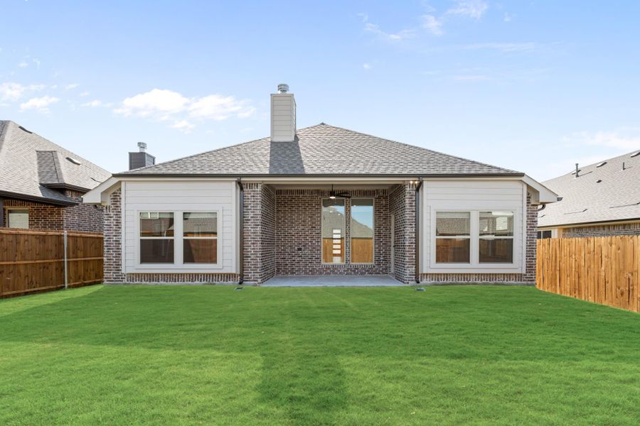 Rear exterior of single-story brick home with covered patio, chimney, and fenced backyard with green lawn Rear exterior of single-story brick home with covered patio, chimney, and fenced backyard with green lawn