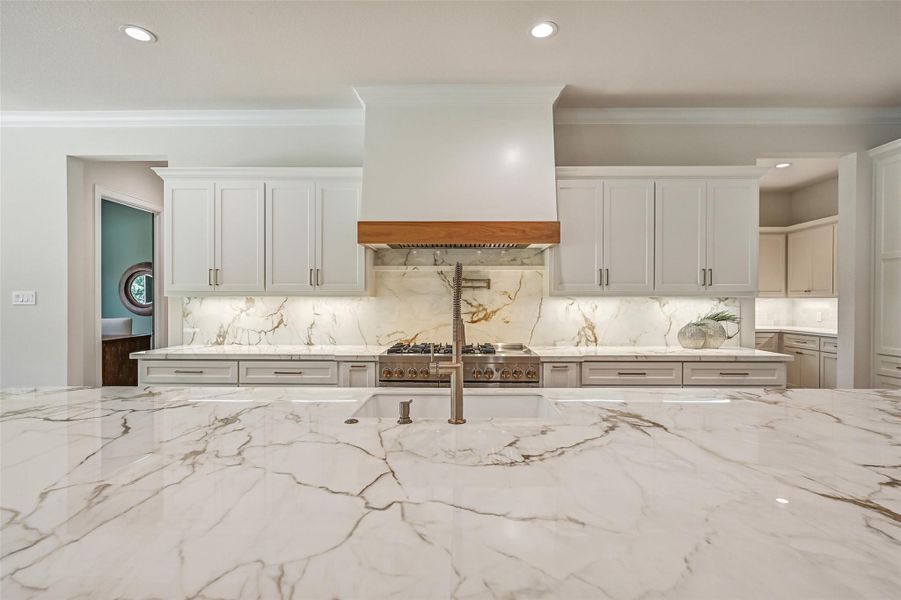 A close-up beautifully showcases the dramatic veining of the Calacatta Macchia Vecchia porcelain across the oversized island, while openings on both sides of the cooking wall provide convenient access to the incredible prep kitchen tucked behind it.