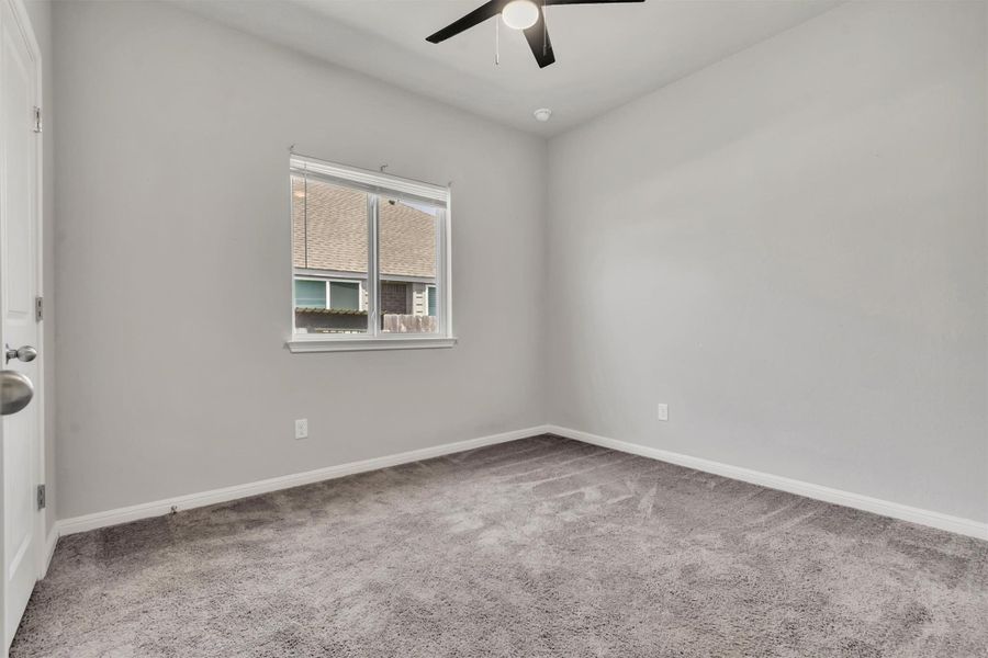 A well-lit bedroom featuring soft carpeting and a ceiling fan for comfort.