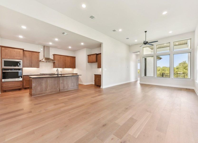 Kitchen featuring wall chimney exhaust hood, brown cabinetry, a ceiling fan, visible vents, and stainless steel appliances Kitchen featuring wall chimney exhaust hood, brown cabinetry, a ceiling fan, visible vents, and stainless steel appliances