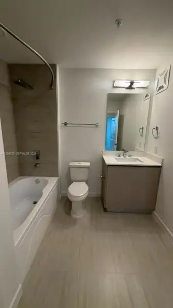 Bathroom featuring large-format tile flooring, a bathtub with a tiled surround, a vanity with a rectangular sink, a light-toned countertop, and a wall-mounted light fixture