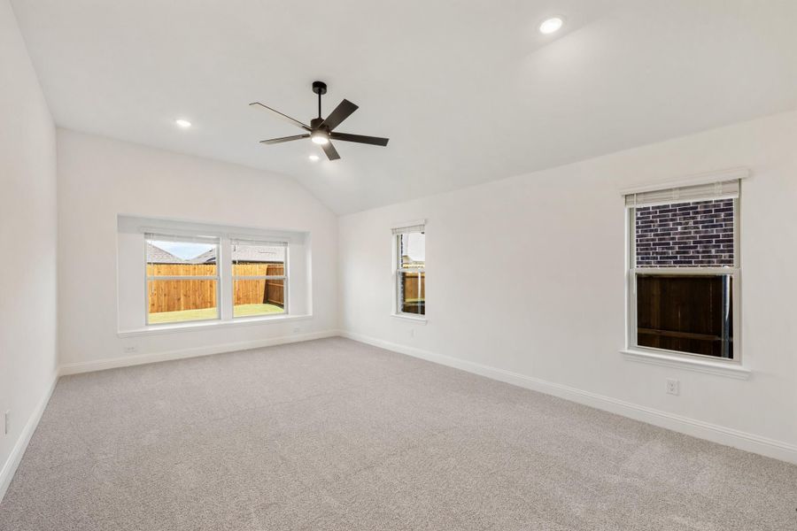 Empty bedroom with gray carpet, vaulted ceiling, ceiling fan, and multiple windows with backyard view Empty bedroom with gray carpet, vaulted ceiling, ceiling fan, and multiple windows with backyard view
