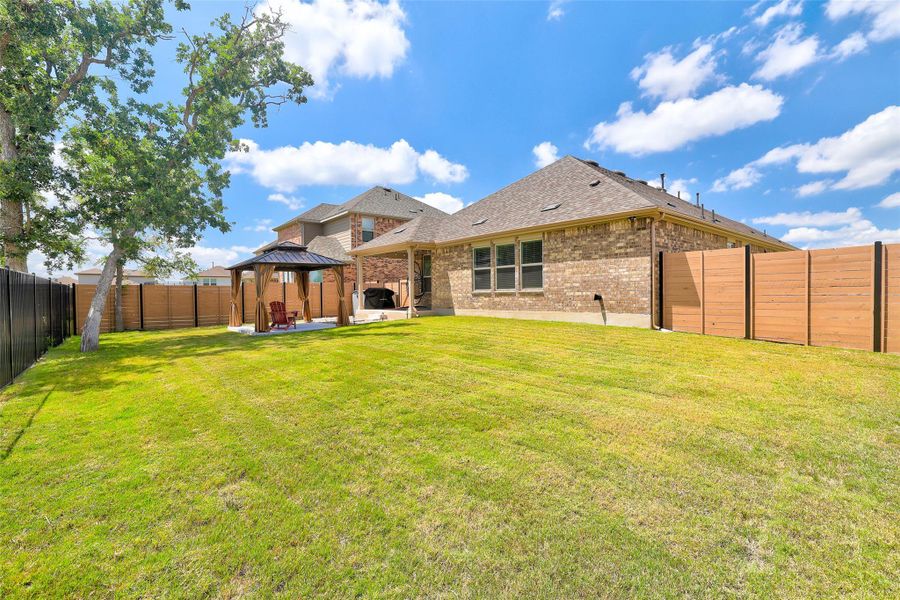 Back of property featuring a gazebo, a patio, brick siding, a fenced backyard, and a shingled roof