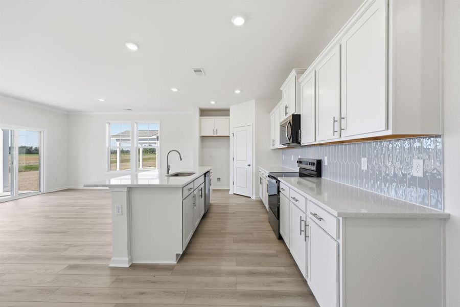 Kitchen featuring white cabinets, appliances with stainless steel finishes, a center island with sink, tasteful backsplash, and light stone counters