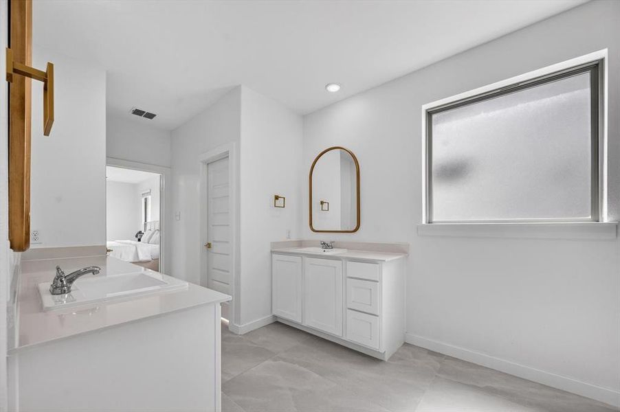 Bright bathroom featuring dual vanity spaces with undermount sinks, white cabinetry, and light-toned countertops