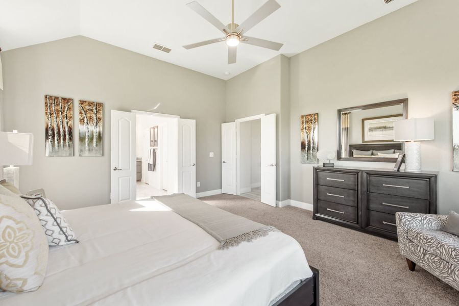 Master bedroom with vaulted ceiling, ceiling fan, dark wood dresser, and carpet flooring with ensuite bathroom access.