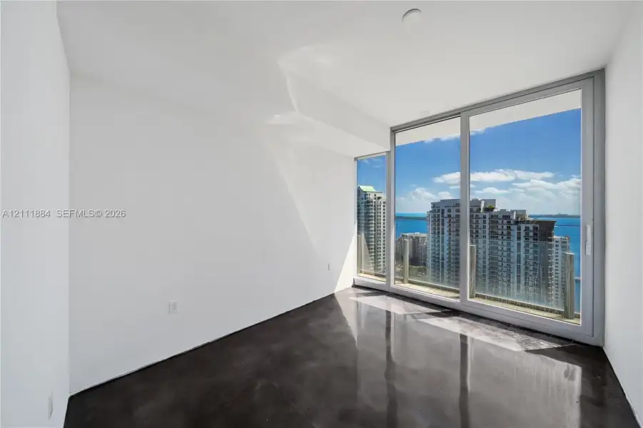 Floor-to-ceiling glass sliding doors, polished concrete flooring, and expansive water and urban skyline backdrop Floor-to-ceiling glass sliding doors, polished concrete flooring, and expansive water and urban skyline backdrop