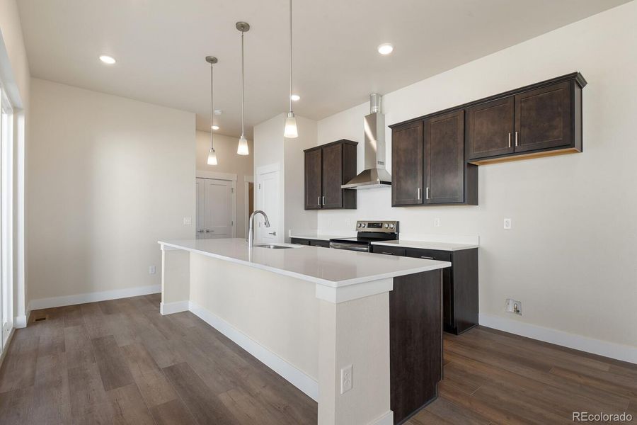 Kitchen features a large center island, quartz countertops, stainless steel appliances, pantry storage, and a hood vent