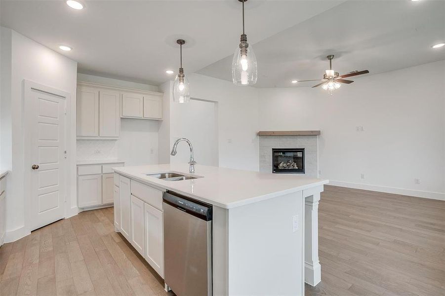 Kitchen featuring light hardwood / wood-style floors, stainless steel dishwasher, a tiled fireplace, sink, and ceiling fan