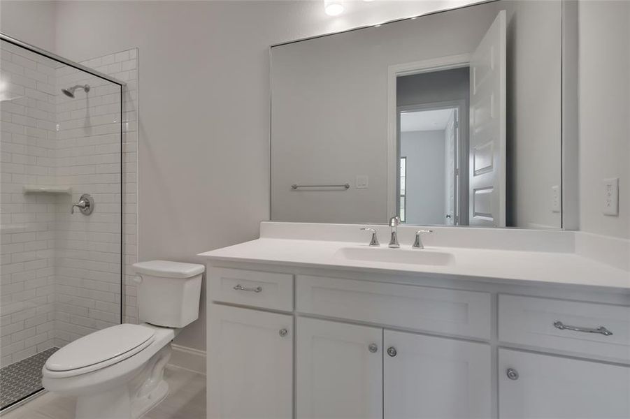 Bathroom with toilet, a tile shower, and vanity