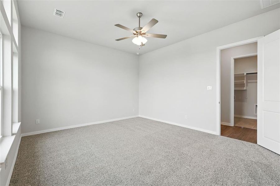 Unfurnished bedroom with carpet, a ceiling fan, and a walk in closet Unfurnished bedroom with carpet, a ceiling fan, and a walk in closet