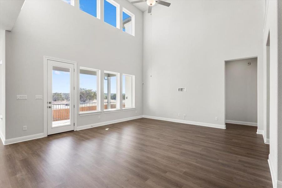 Unfurnished living room featuring ceiling fan, dark wood-type flooring, and a high ceiling