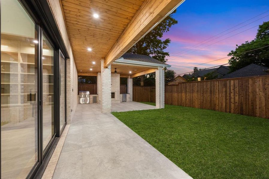 The property features a covered patio with a wooden ceiling and recessed lighting, extending to a grassy yard