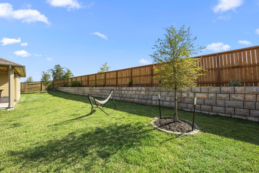 The spacious, fully stained fenced backyard with a retaining wall, providing additional space for gardening, landscaping, or enjoying outdoor games.