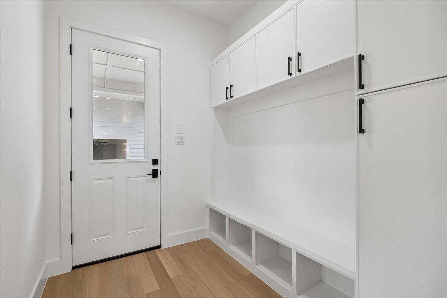 A built-in mudroom area near the secondary entry adds practical storage and organization with custom bench seating, upper cabinetry, hanging space, and additional room for everyday functionality. Positioned just off the main living areas, the space helps create separation for daily routines while maintaining the home’s clean architectural aesthetic.