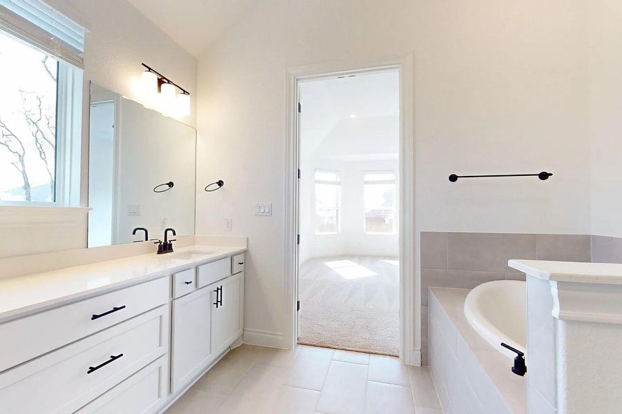 Bathroom featuring a white vanity with a large mirror, a built-in bathtub, and light-colored tile flooring