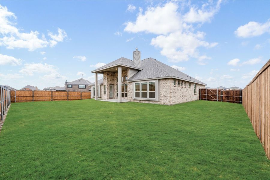 Backyard of brick home with large green lawn, covered patio, and wood privacy fence