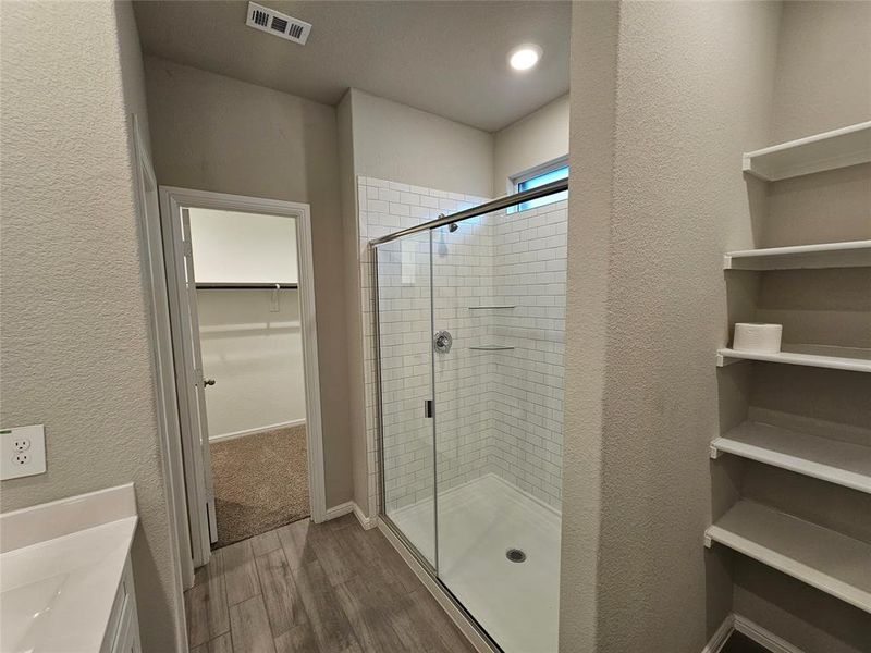 Full bathroom with a spacious closet, double sink, a stall shower, wood-looking tile flooring.