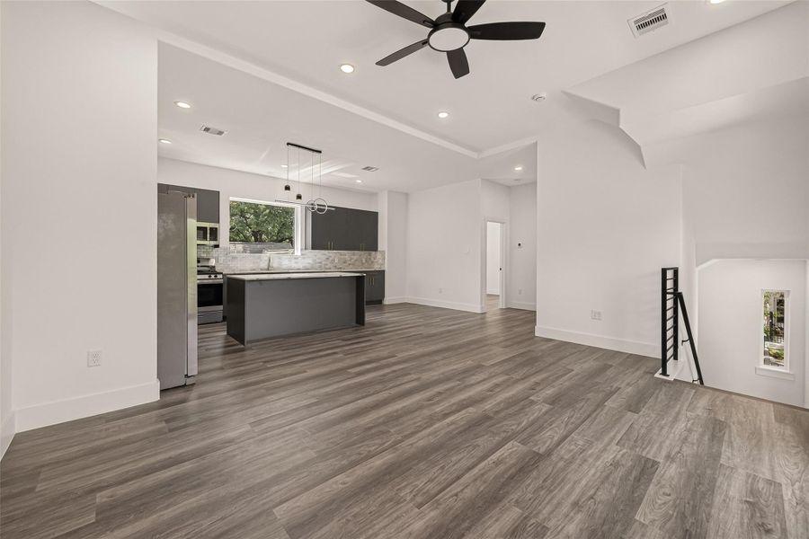 This modern open-concept living area features sleek vinyl flooring, a stylish ceiling fan, and ample natural light. The kitchen offers dark cabinetry, stainless steel appliances, and a central island with contemporary lighting, perfect for both cooking and entertaining. This modern open-concept living area features sleek vinyl flooring, a stylish ceiling fan, and ample natural light. The kitchen offers dark cabinetry, stainless steel appliances, and a central island with contemporary lighting, perfect for both cooking and entertaining.