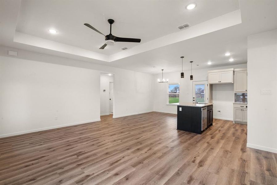 Kitchen featuring a center island with sink, a raised ceiling, and white cabinetry Kitchen featuring a center island with sink, a raised ceiling, and white cabinetry