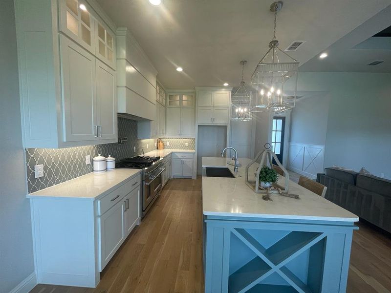 Kitchen with a sink, double oven range, custom exhaust hood, white cabinetry, and recessed lighting Kitchen with a sink, double oven range, custom exhaust hood, white cabinetry, and recessed lighting