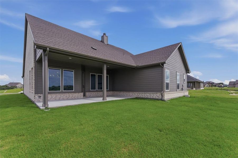 Expansive green lawn surrounds a residence featuring a covered patio with gray siding and stone wainscoting Expansive green lawn surrounds a residence featuring a covered patio with gray siding and stone wainscoting