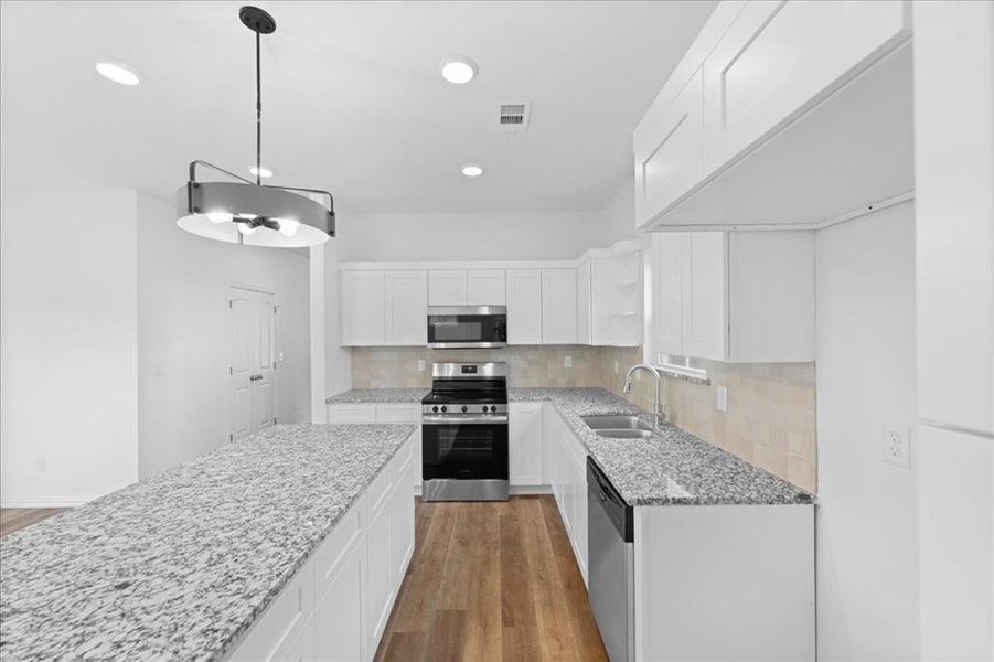 Modern kitchen featuring granite countertops, white shaker cabinetry, stainless steel appliances, and tile backsplash. Large center island provides ample prep space and additional seating.