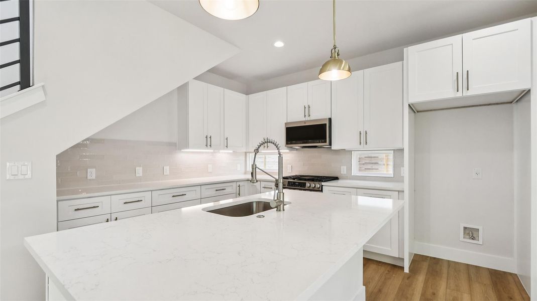 Kitchen with white cabinets, light stone counters, light wood-type flooring, appliances with stainless steel finishes, and decorative light fixtures Kitchen with white cabinets, light stone counters, light wood-type flooring, appliances with stainless steel finishes, and decorative light fixtures