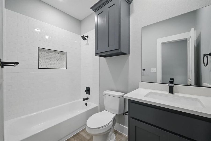 Bathroom featuring toilet, wood finished floors, vanity, shower / bath combination, and baseboards