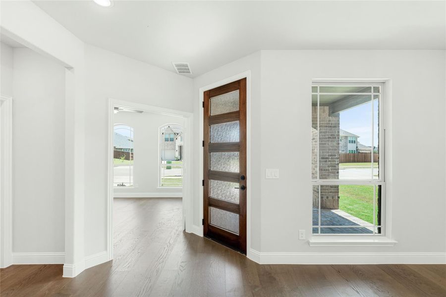 Entryway with dark wood front door with glass panels, hardwood floors, and white walls Entryway with dark wood front door with glass panels, hardwood floors, and white walls