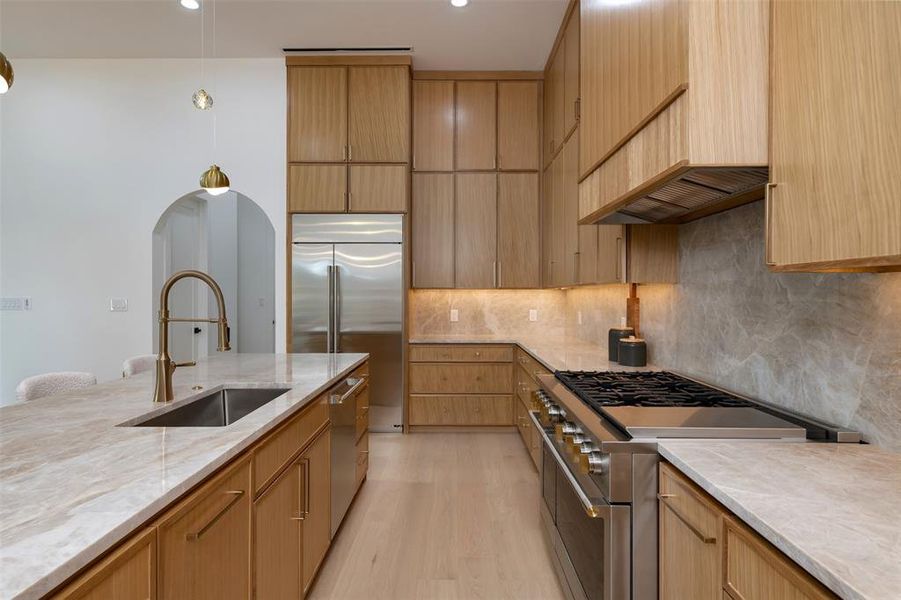 Kitchen with high quality appliances, light stone countertops, light wood-type flooring, backsplash, and premium range hood Kitchen with high quality appliances, light stone countertops, light wood-type flooring, backsplash, and premium range hood