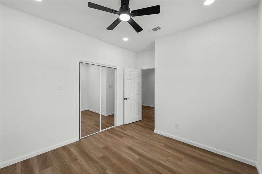 Interior room with wood-finish flooring, white walls, and a black ceiling fan with integrated lighting Interior room with wood-finish flooring, white walls, and a black ceiling fan with integrated lighting