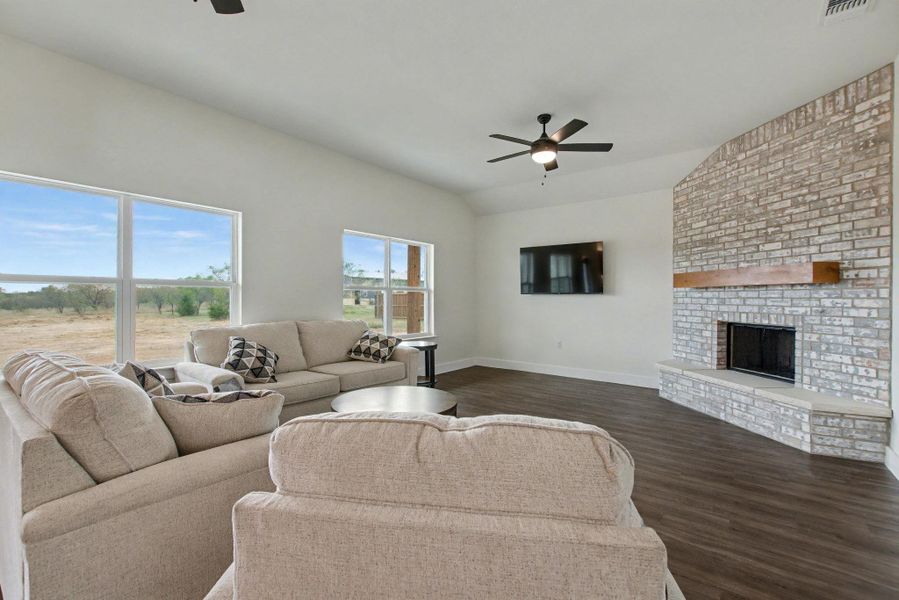 Living room featuring a ceiling fan, dark wood-type flooring, vaulted ceiling, and a fireplace