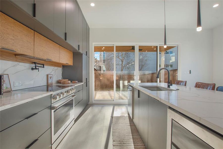 Kitchen featuring gray cabinetry, sink, stainless steel appliances, tasteful backsplash, and pendant lighting