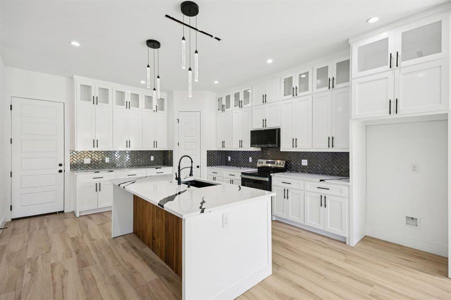 Kitchen with glass insert cabinets, appliances with stainless steel finishes, white cabinets, a kitchen island with sink, and light stone counters