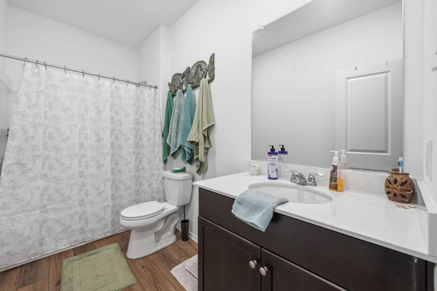 Full bathroom featuring wood-finish flooring, a white toilet, and a vanity with a white countertop and dark wood-finish cabinetry