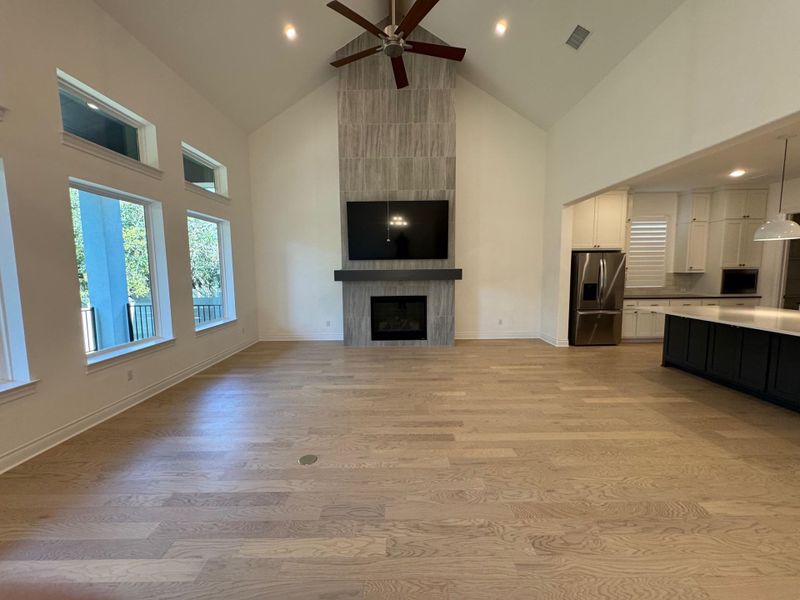 Open concept living room with high vaulted ceiling, light wood-style floors, a tiled gas log fireplace, a ceiling fan, and recessed lighting