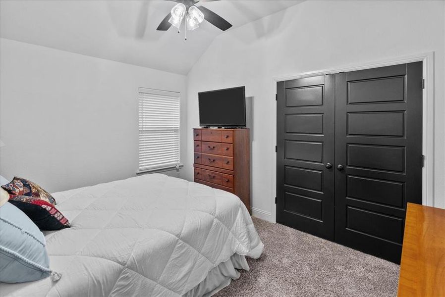 Carpeted bedroom featuring ceiling fan and vaulted ceiling