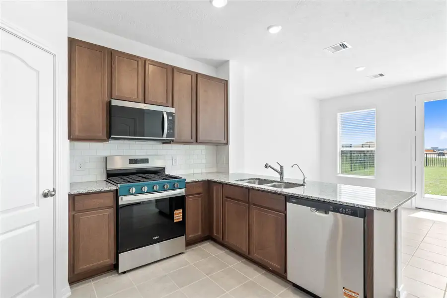 This spacious kitchen boasts soaring ceilings, Woodmont Cody cabinets in Ginger stain, Granite Luna Pearl countertops, stainless steel Whirlpool appliances, a modern Daltile backsplash, recessed lighting, and a pantry—all overlooking the expansive Great Room. This spacious kitchen boasts soaring ceilings, Woodmont Cody cabinets in Ginger stain, Granite Luna Pearl countertops, stainless steel Whirlpool appliances, a modern Daltile backsplash, recessed lighting, and a pantry—all overlooking the expansive Great Room.
