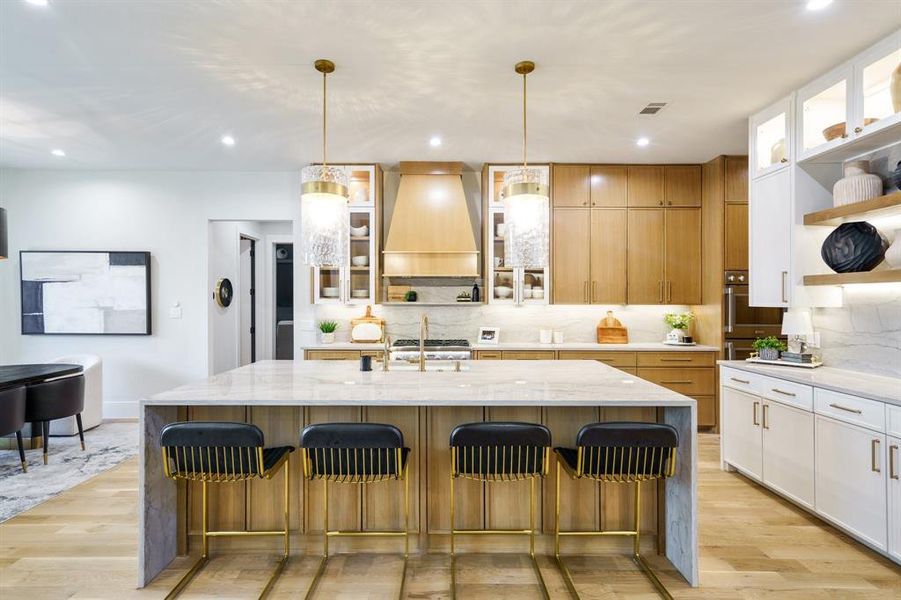 Kitchen with custom exhaust hood, a center island with sink, light stone countertops, light hardwood / wood-style floors, and white cabinets