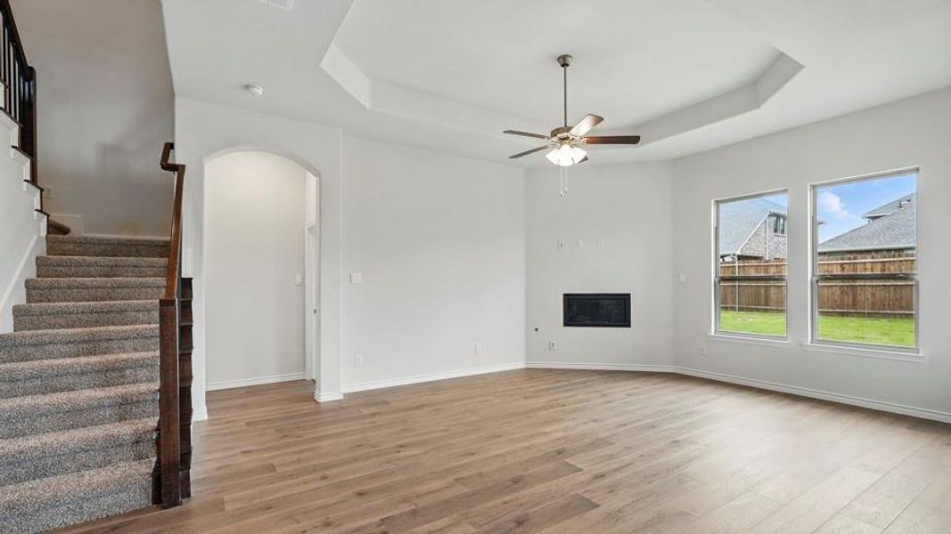 Spacious interior featuring wood-finish flooring, a contemporary fireplace, and a tray ceiling with a ceiling fan