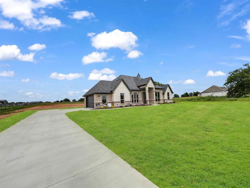 French country home with stone siding, a front yard, and driveway