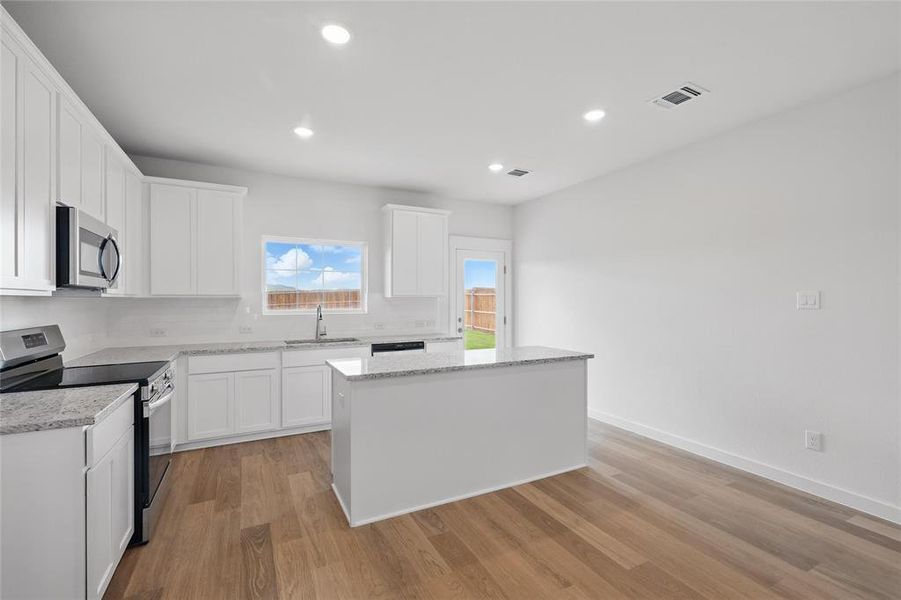 Kitchen featuring stainless steel appliances, a sink, tasteful backsplash, light wood-style floors, and a kitchen island Kitchen featuring stainless steel appliances, a sink, tasteful backsplash, light wood-style floors, and a kitchen island