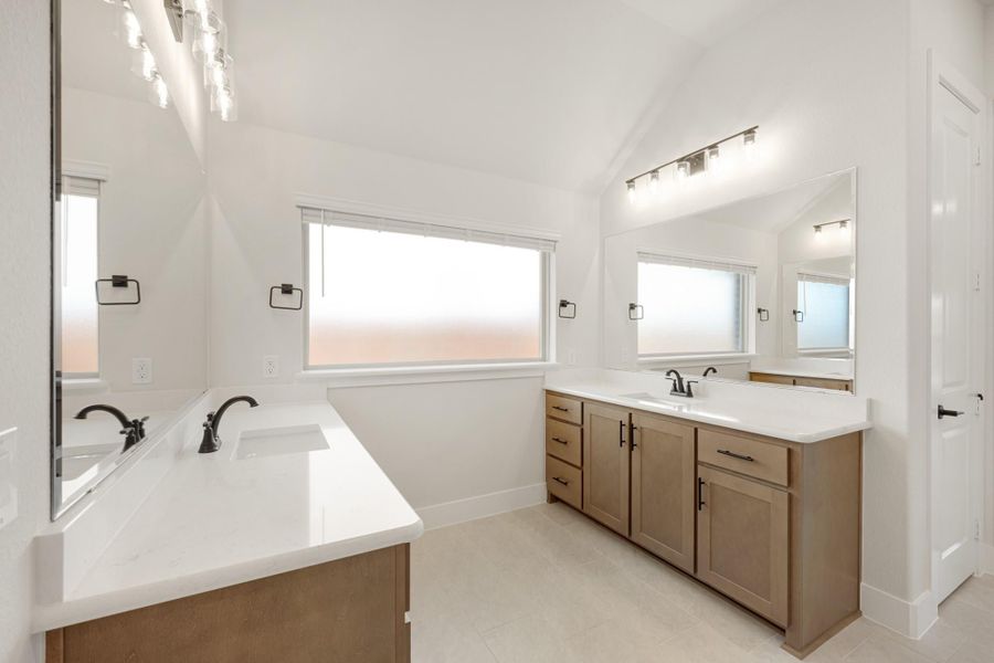 Bathroom with dual vanities, wood cabinets, white countertops, and large mirrors with overhead lighting