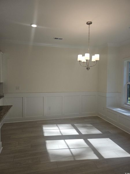 Unfurnished dining area with a decorative wall, light wood-type flooring, a wainscoted wall, a chandelier, and ornamental molding Unfurnished dining area with a decorative wall, light wood-type flooring, a wainscoted wall, a chandelier, and ornamental molding