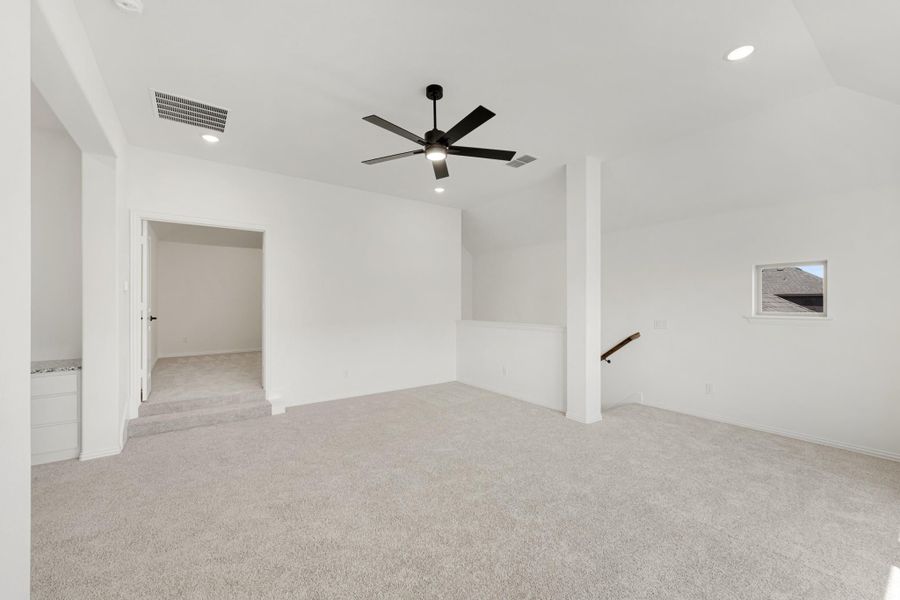 Open upstairs loft with carpet flooring, black ceiling fan, and staircase railing near small window