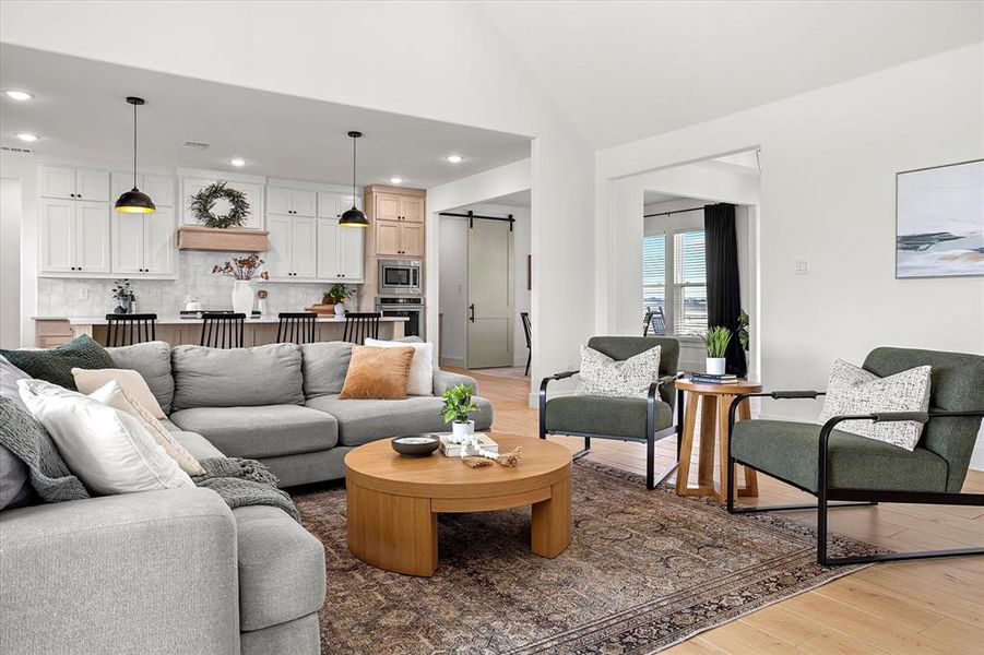 Living room with a barn door, light hardwood / wood-style flooring, and high vaulted ceiling