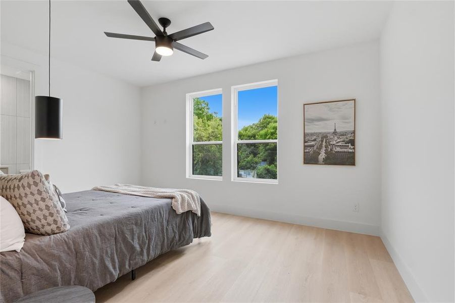 Bedroom featuring light wood-finish flooring, white walls, and two large windows Bedroom featuring light wood-finish flooring, white walls, and two large windows